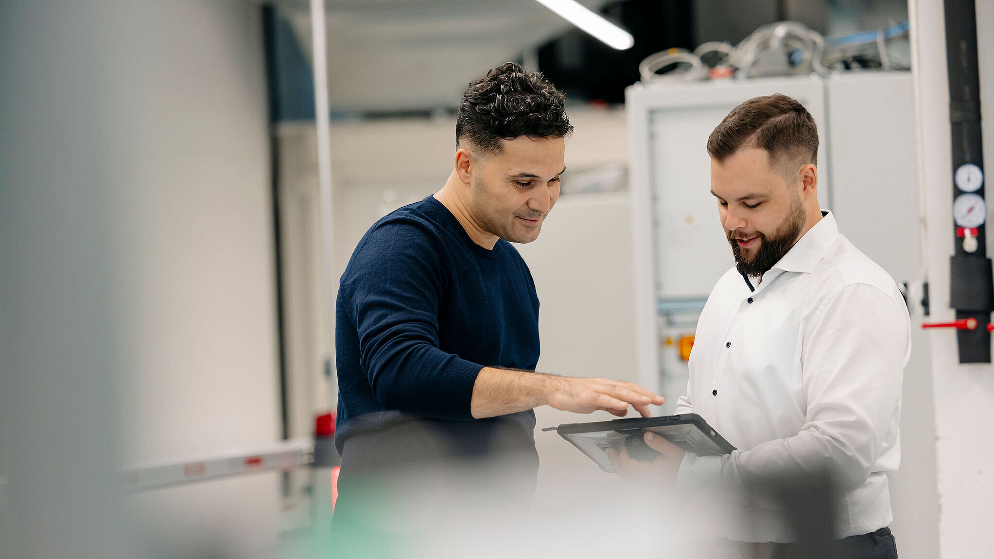 Zwei Personen stehen in einer technischen Umgebung zusammen und besprechen Informationen auf einem Tablet.