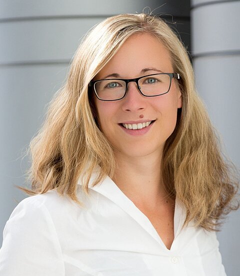 Eine Frau mit blonden Haaren und Brille lächelt in die Kamera.