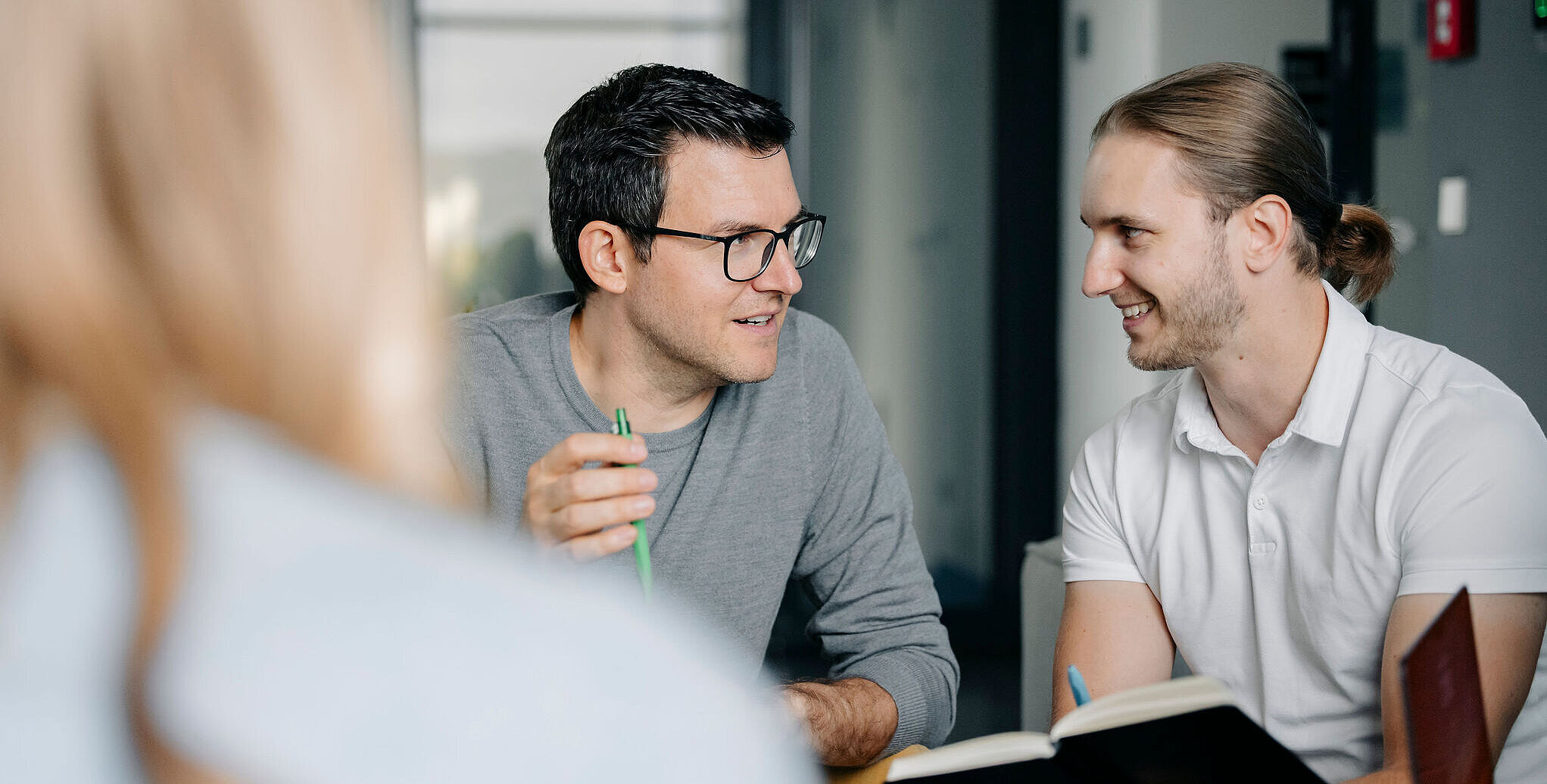 Mehrere Personen sitzen zusammen im Gespräch und besprechen projektbezogene Aufgaben in einer kollaborativen Arbeitsumgebung.