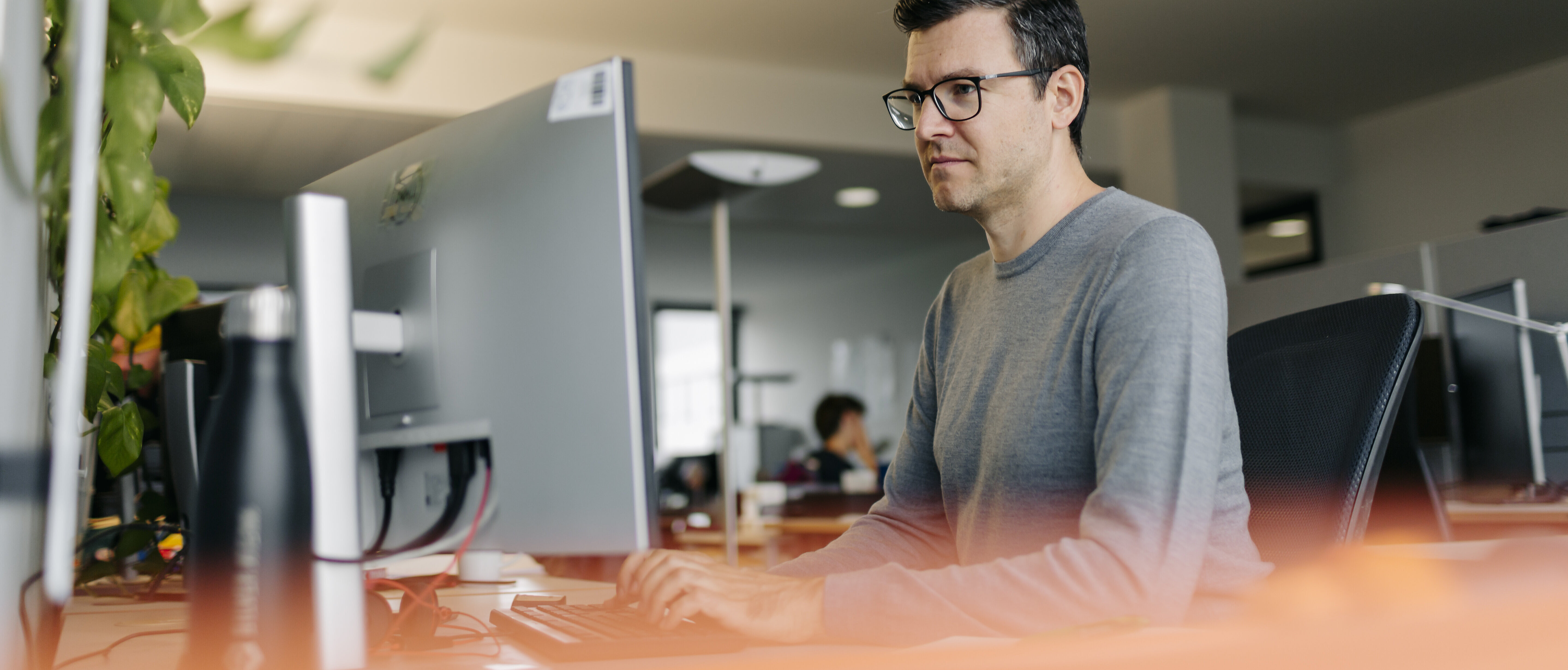 Mann mit Brille arbeitet konzentriert am Computer in einem modernen Büro.