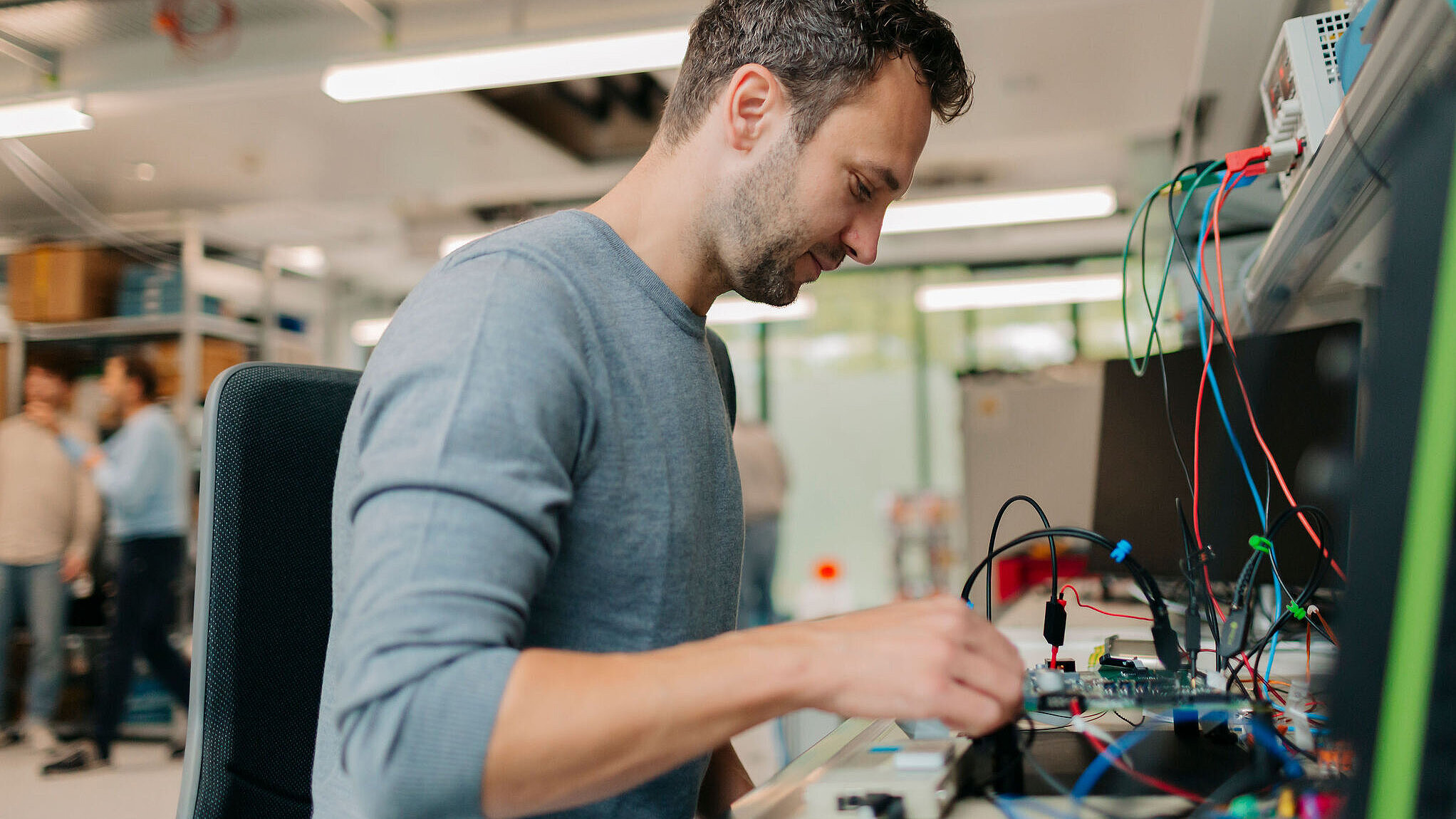 Ein Mann arbeitet konzentriert an einem Prüfstand mit vielen Kabeln und elektronischen Bauteilen in einem Labor.