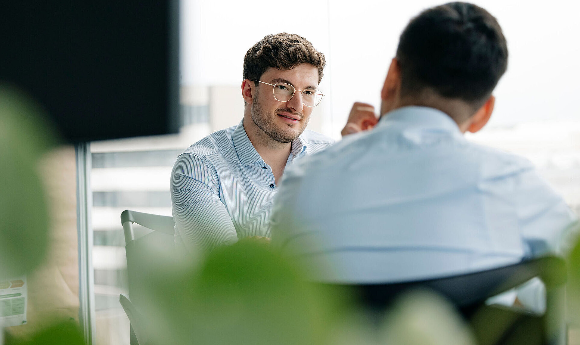 Zwei Personen sitzen sich in einem Meeting gegenüber und besprechen projektbezogene Aufgaben in einem modernen Büro.