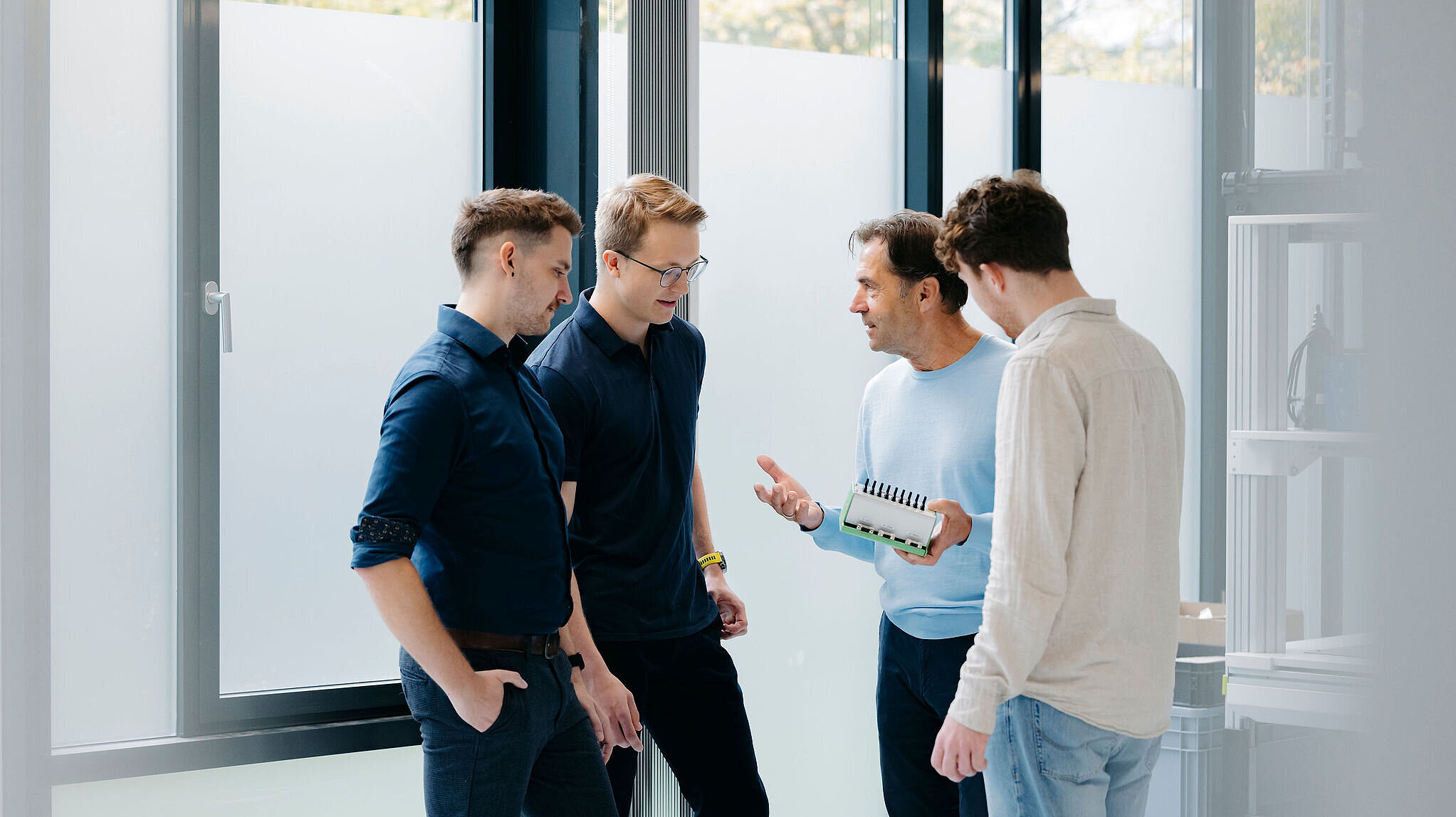 Vier Kollegen stehen zusammen und besprechen ein technisches Gerät, das einer von ihnen in der Hand hält.