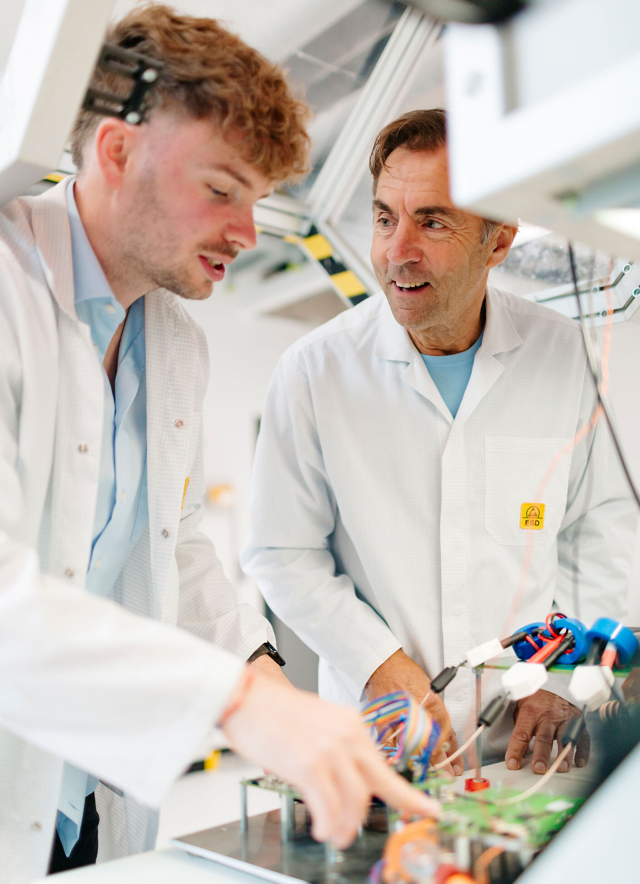 Zwei Personen in Laborkleidung arbeiten gemeinsam an einer elektronischen Baugruppe und besprechen die nächsten Arbeitsschritte.