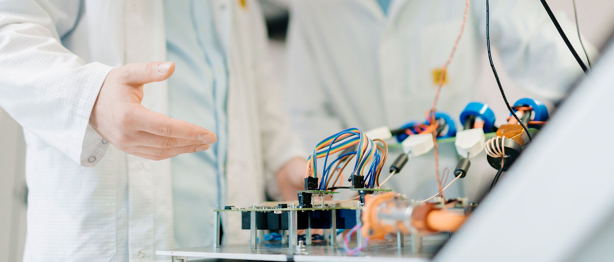 Zwei Personen in ESD-Kitteln arbeiten an einem Prüfstand mit vielen Kabeln und elektronischen Bauteilen.