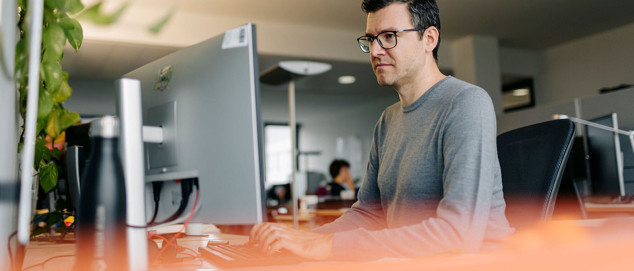 Mann mit Brille arbeitet konzentriert am Computer in einem modernen Büro.