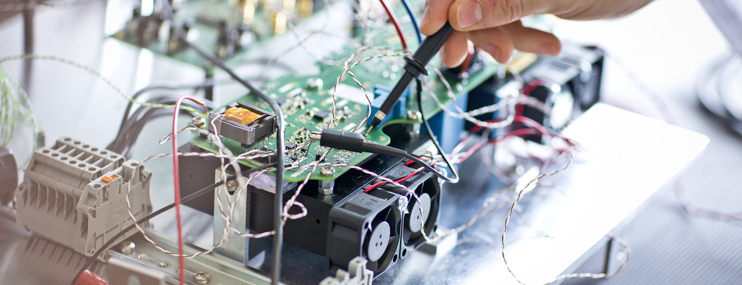 Nahaufnahme einer elektronischen Baugruppe, an der eine Person mit Messspitzen arbeitet.