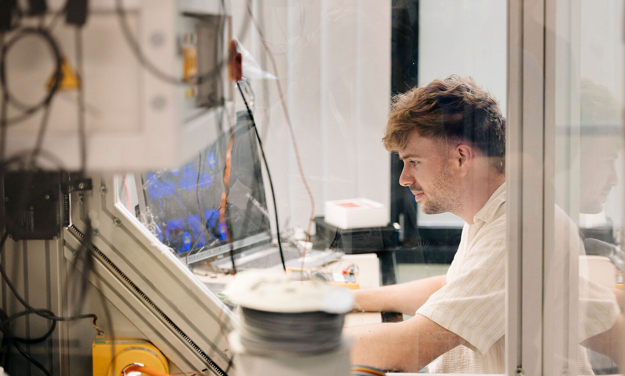 Person arbeitet konzentriert an einem Computer in einer technischen Testumgebung, umgeben von Messgeräten und Kabeln.