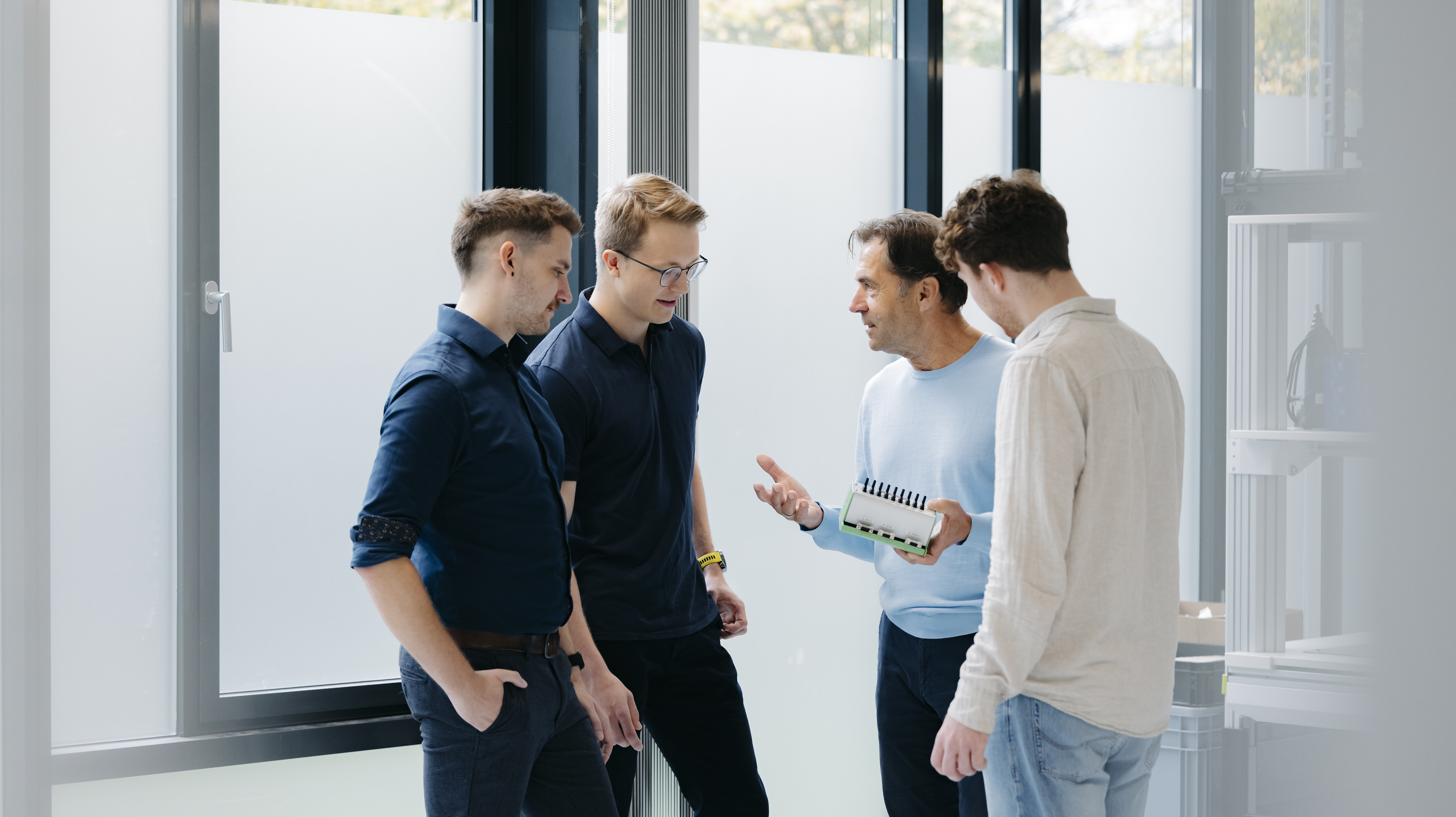 Vier Kollegen stehen zusammen und besprechen ein technisches Gerät, das einer von ihnen in der Hand hält.