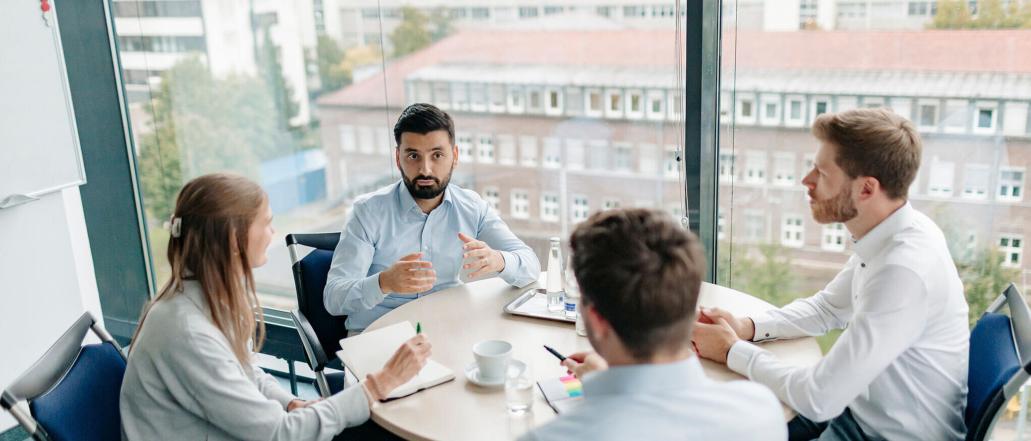 Vier Personen sitzen in einem Besprechungsraum und führen ein Gespräch an einem runden Tisch.