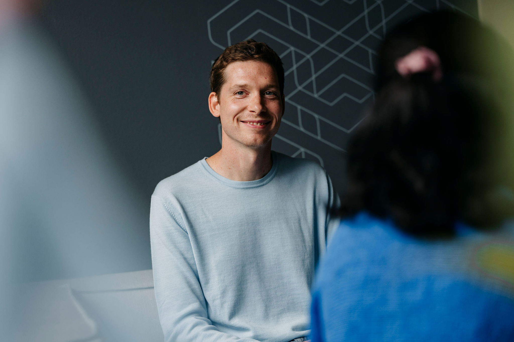 Person sitzt lächelnd in einem Gespräch in einem modernen, entspannten Arbeitsumfeld.