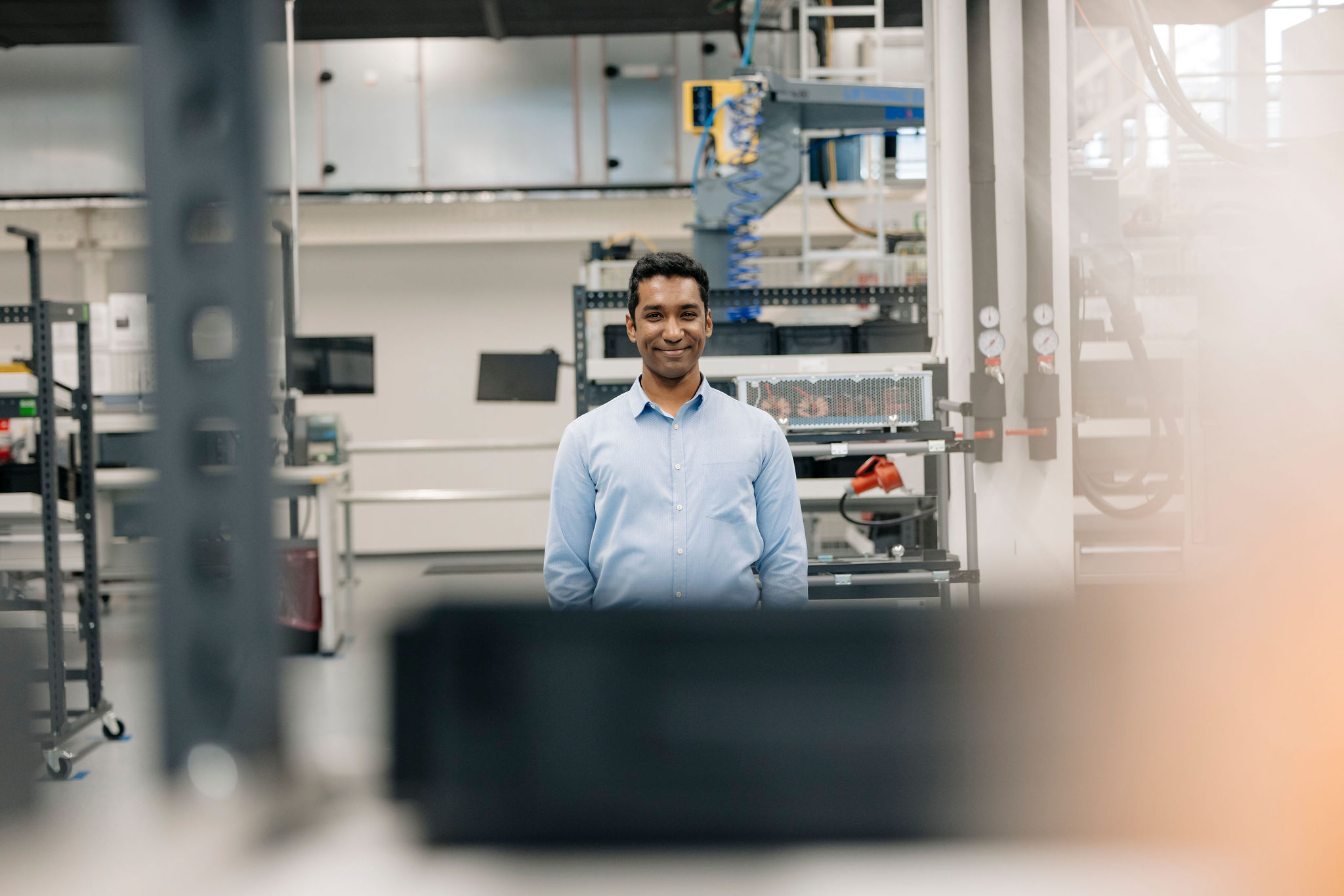 Person steht lächelnd in einer Produktionshalle und blickt in die Kamera.