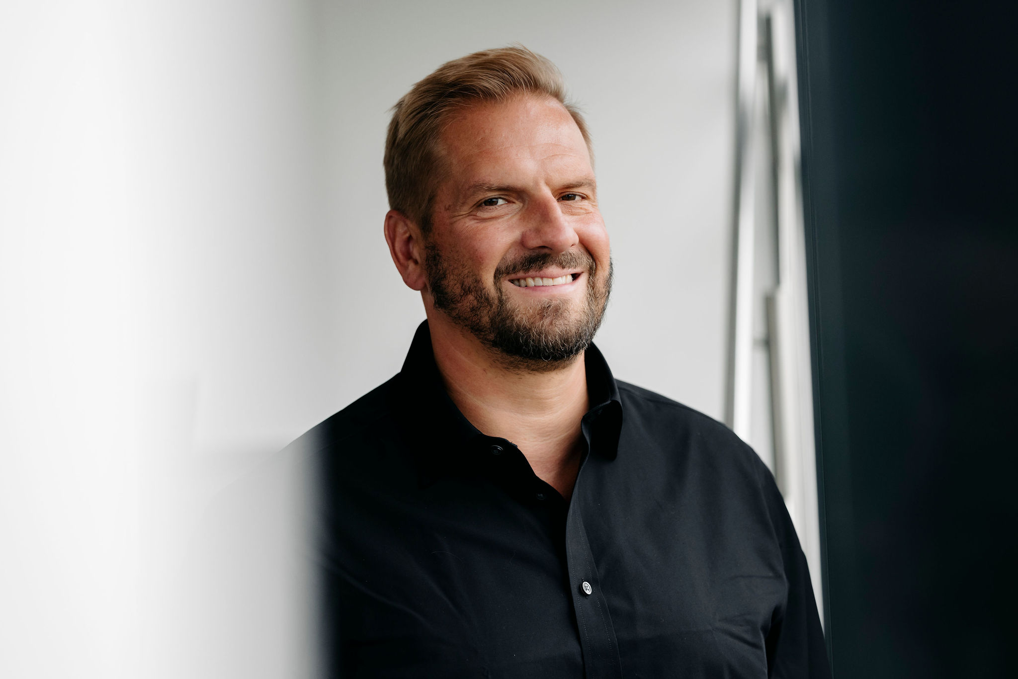 Person steht lächelnd in einem hellen Raum und blickt freundlich in Richtung Kamera.