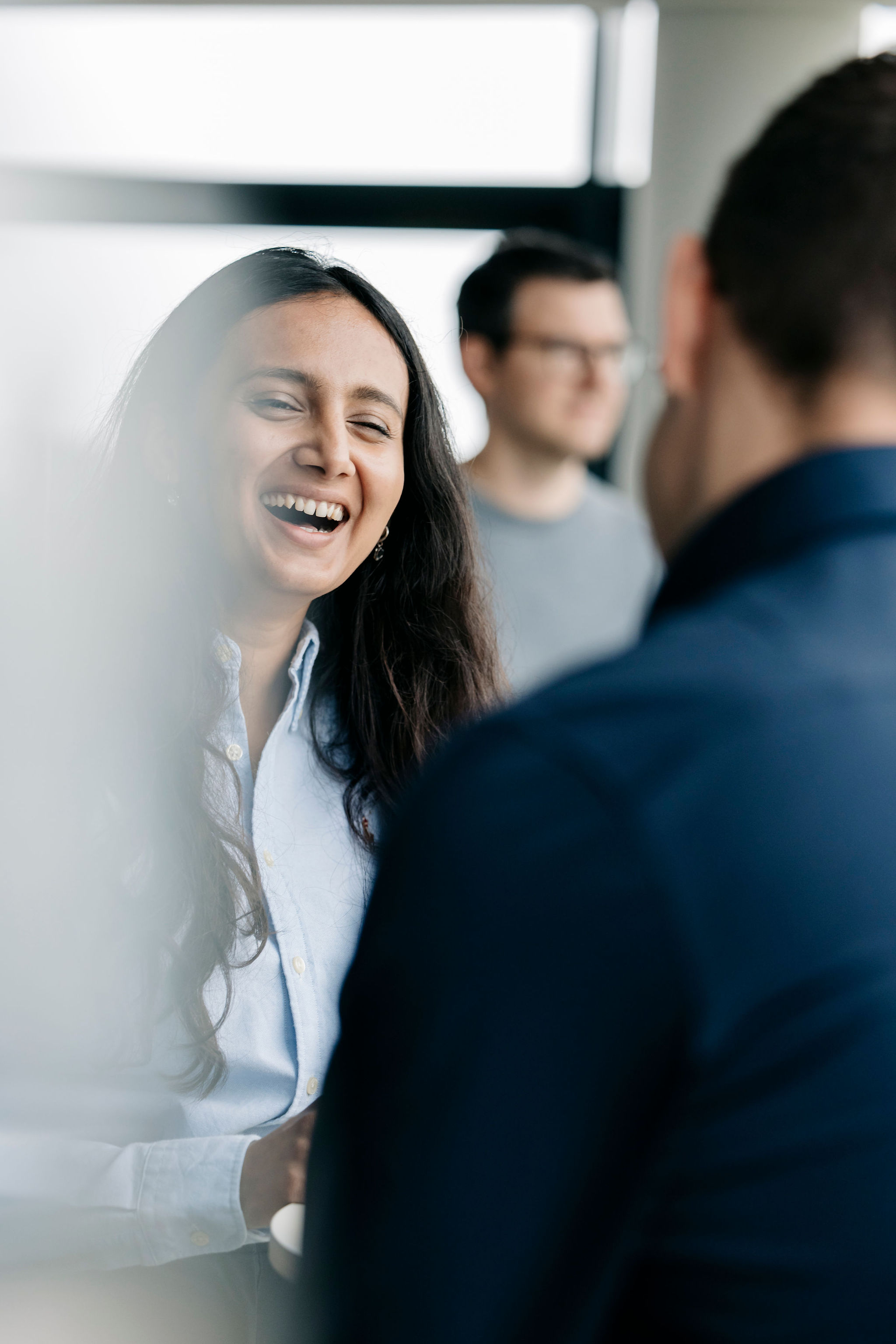 Lachende Frau im Gespräch mit Kolleginnen und Kollegen in einer Bürosituation.