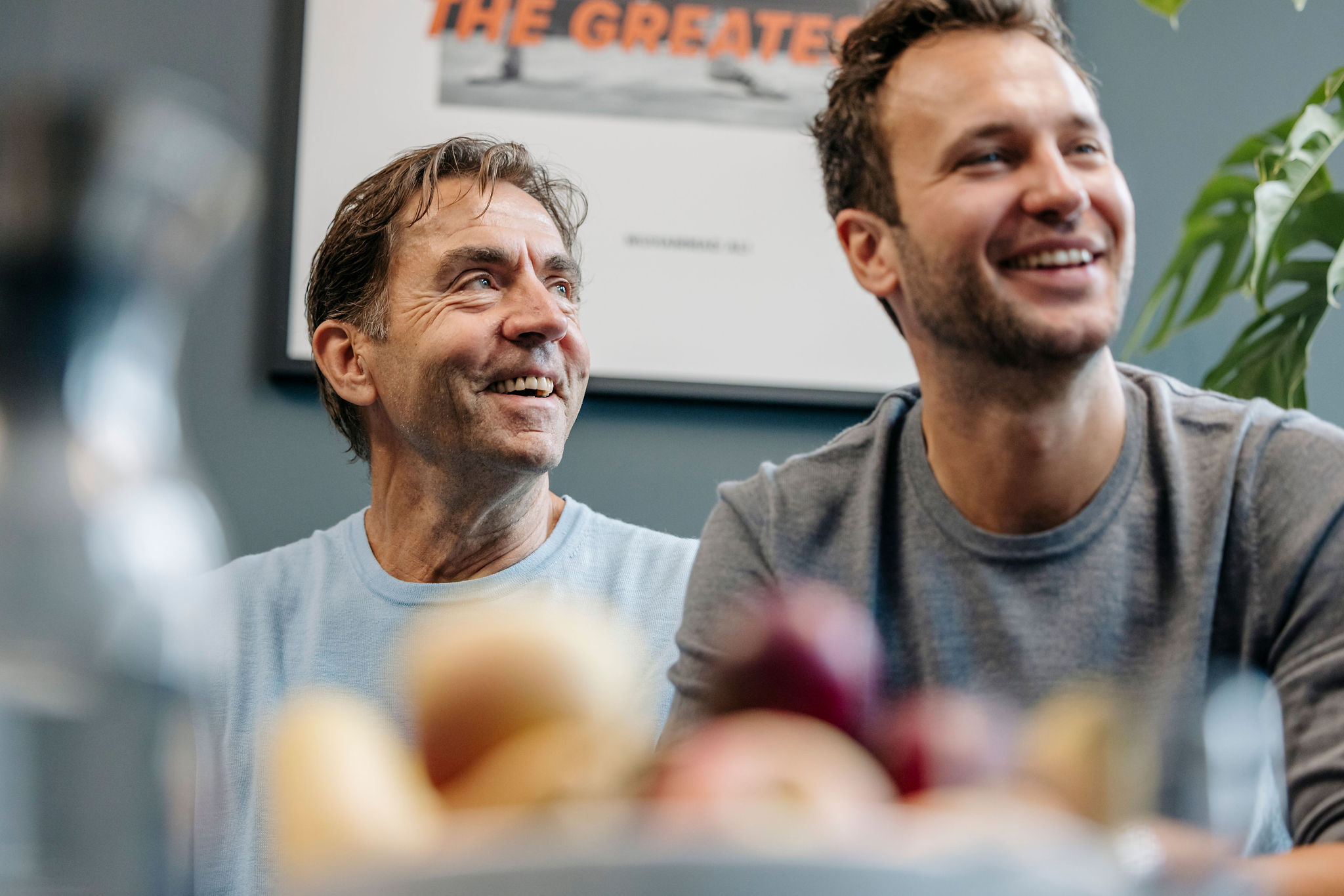 Zwei Personen sitzen nebeneinander, lächeln und wirken in ein Gespräch vertieft.